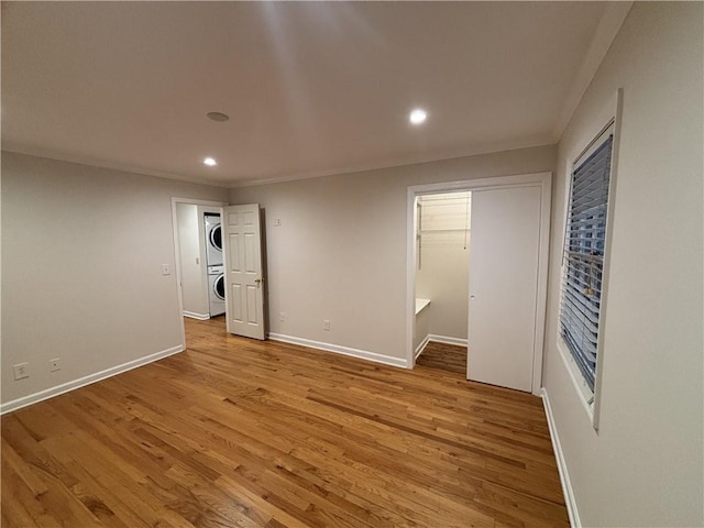 unfurnished bedroom featuring stacked washer / drying machine, recessed lighting, light wood finished floors, ornamental molding, and baseboards