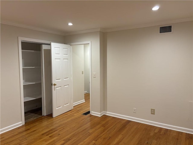 unfurnished bedroom featuring light wood finished floors, crown molding, recessed lighting, baseboards, and a closet
