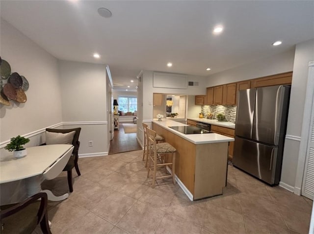 kitchen featuring freestanding refrigerator, a kitchen breakfast bar, a peninsula, brown cabinetry, and light countertops