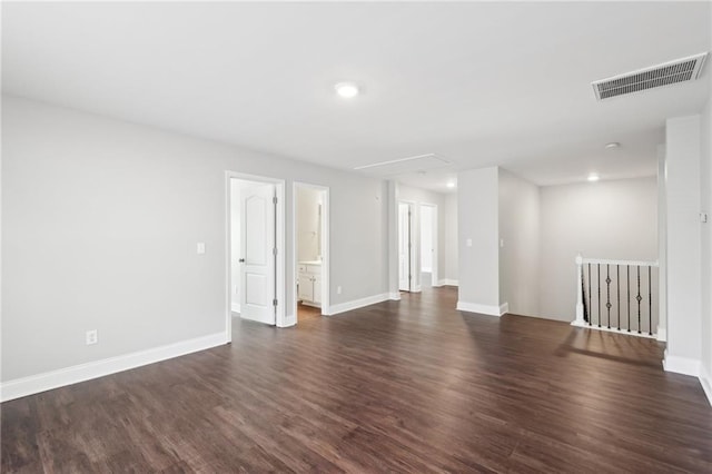 unfurnished room with attic access, baseboards, dark wood-style flooring, and visible vents