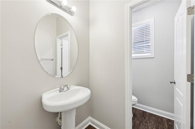 half bath with toilet, wood finished floors, and baseboards