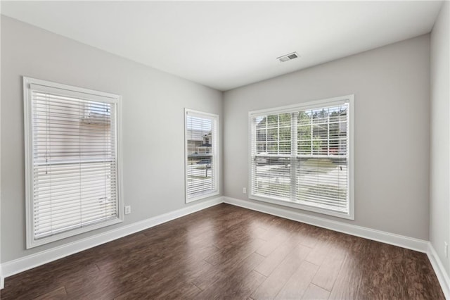 spare room featuring baseboards, dark wood-type flooring, and visible vents