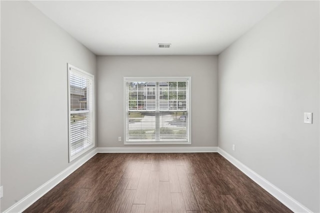 spare room with dark wood finished floors, visible vents, and baseboards