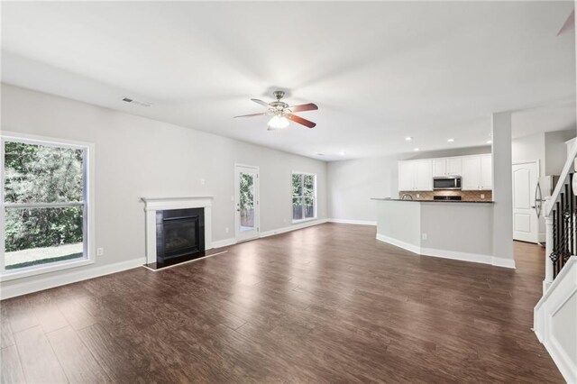 unfurnished living room featuring recessed lighting, dark wood finished floors, stairway, a glass covered fireplace, and ceiling fan