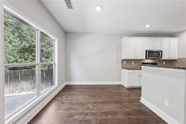 kitchen with stainless steel microwave, tasteful backsplash, white cabinets, and baseboards
