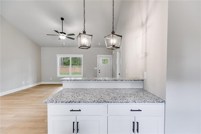 kitchen with light stone counters, light wood-type flooring, white cabinets, and decorative light fixtures