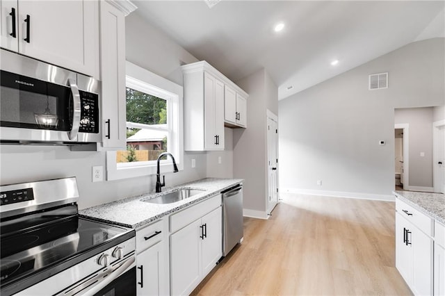 kitchen featuring visible vents, white cabinets, vaulted ceiling, stainless steel appliances, and a sink