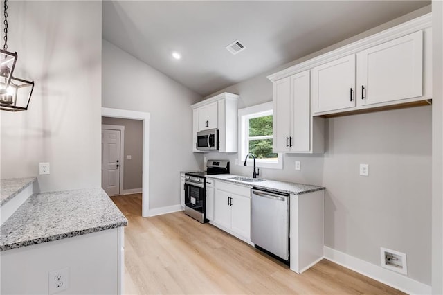 kitchen with lofted ceiling, light wood-style flooring, stainless steel appliances, a sink, and white cabinets