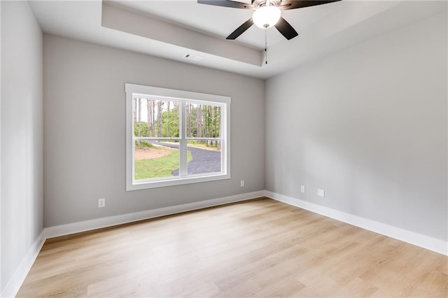 empty room with a raised ceiling, visible vents, baseboards, and wood finished floors