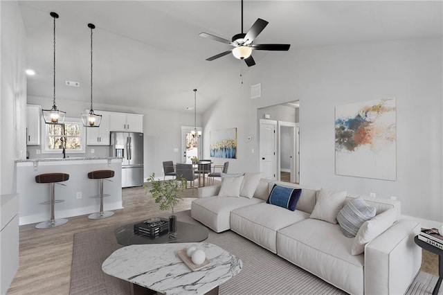 living room with light wood finished floors, visible vents, high vaulted ceiling, and ceiling fan with notable chandelier