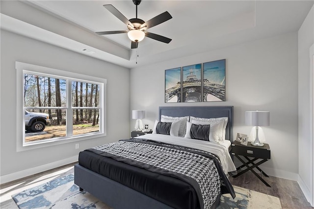 bedroom with a tray ceiling, visible vents, ceiling fan, wood finished floors, and baseboards