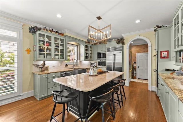 kitchen featuring arched walkways, built in appliances, a sink, and ornamental molding