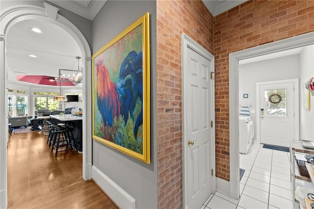 corridor with brick wall, washing machine and clothes dryer, baseboards, and light tile patterned floors