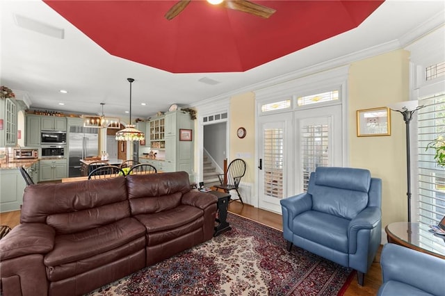 living room with crown molding, wood finished floors, a ceiling fan, and stairway