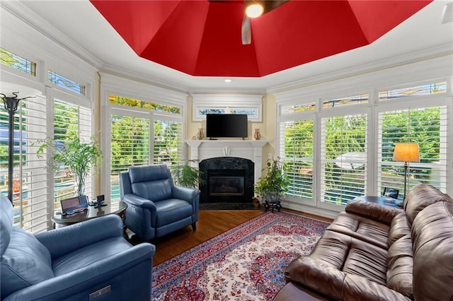 living area with a fireplace with flush hearth, a healthy amount of sunlight, wood finished floors, and ornamental molding