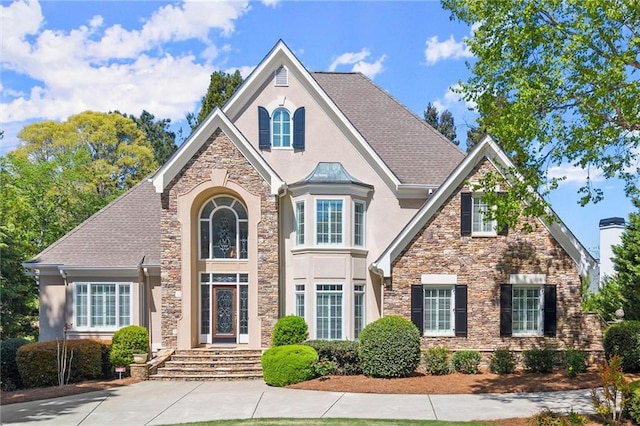 view of front of property with a shingled roof, stucco siding, and stone siding