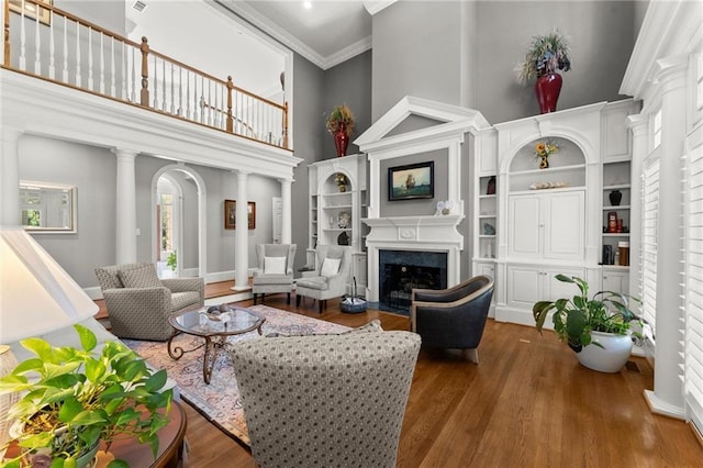 living room featuring a high ceiling, decorative columns, crown molding, wood finished floors, and a fireplace with flush hearth