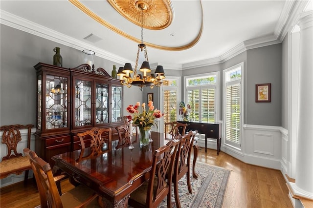 dining room featuring crown molding, visible vents, a wainscoted wall, a chandelier, and wood finished floors