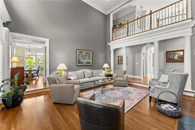 living area with crown molding, ornate columns, wood finished floors, and a towering ceiling