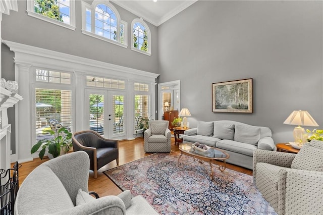 living area with french doors, a high ceiling, crown molding, a fireplace with raised hearth, and wood finished floors