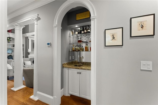 bar featuring indoor wet bar, ornate columns, wood finished floors, and a sink