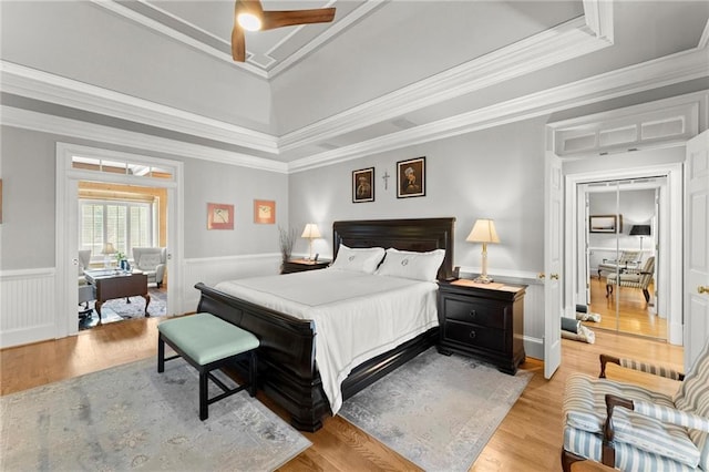 bedroom with crown molding, a raised ceiling, wainscoting, and light wood-style floors