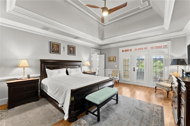bedroom featuring access to exterior, a tray ceiling, crown molding, and wood finished floors