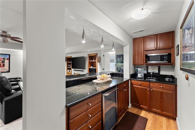 kitchen with dark stone counters, light wood-style flooring, stainless steel microwave, open floor plan, and wine cooler
