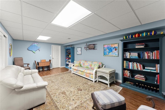 living room featuring a paneled ceiling, baseboards, and wood finished floors
