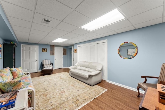 living area with wood finished floors, baseboards, a drop ceiling, and visible vents