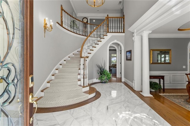 entryway with arched walkways, crown molding, decorative columns, and stairway