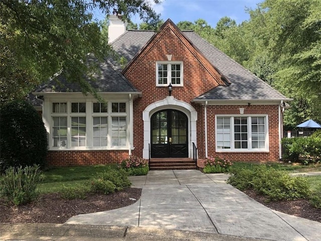 view of front of property featuring brick siding, french doors, a chimney, and a shingled roof