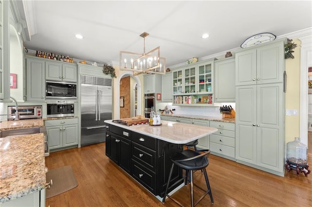 kitchen featuring light wood-style flooring, arched walkways, built in appliances, and an inviting chandelier