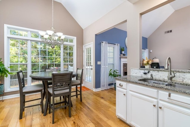 kitchen featuring pendant lighting, sink, white cabinetry, light stone countertops, and a chandelier