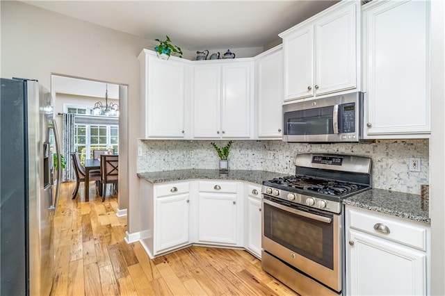 kitchen featuring an inviting chandelier, white cabinetry, appliances with stainless steel finishes, backsplash, and light stone countertops