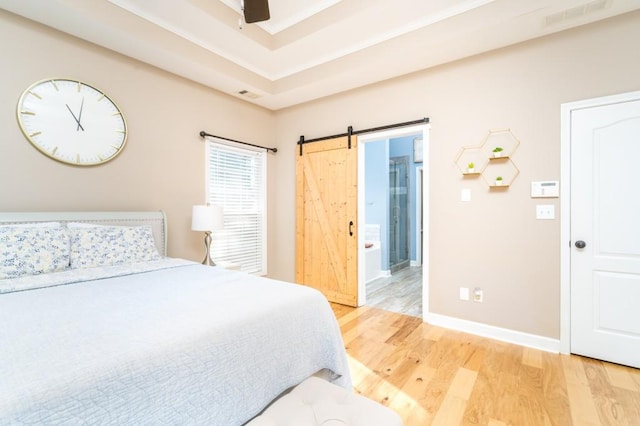 bedroom with ensuite bathroom, a barn door, hardwood / wood-style floors, ceiling fan, and a raised ceiling