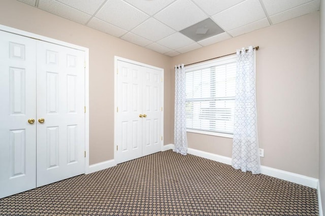 unfurnished bedroom featuring dark carpet and a drop ceiling