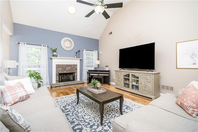 living room featuring ceiling fan, high vaulted ceiling, a stone fireplace, and light hardwood / wood-style flooring