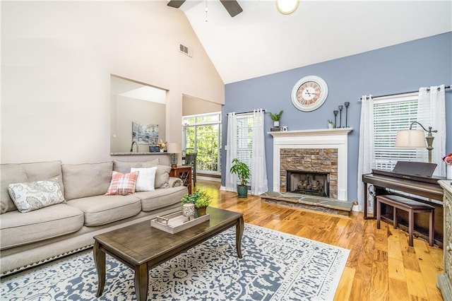 living room featuring light wood-type flooring, ceiling fan, plenty of natural light, and a stone fireplace