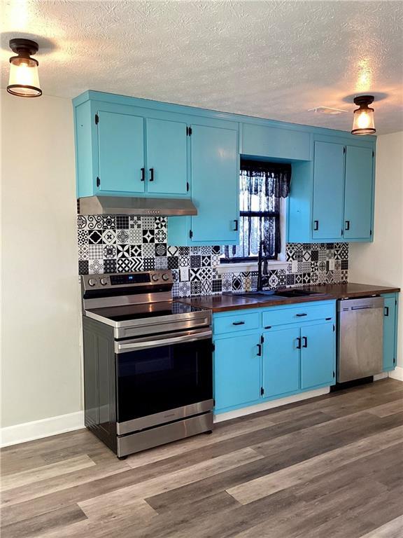 5085 Truman Mountain Rd, Gainesville, GA 30506 - kitchen featuring appliances with stainless steel finishes, blue cabinets, under cabinet range hood, dark countertops, and a textured ceiling