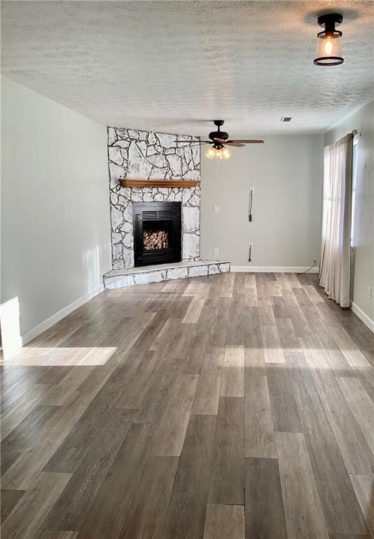 5085 Truman Mountain Rd, Gainesville, GA 30506 - unfurnished living room with a stone fireplace, a textured ceiling, ceiling fan, wood finished floors, and baseboards