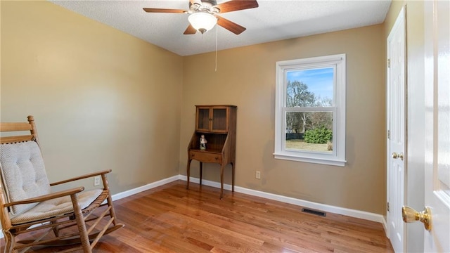 living area featuring light wood finished floors, baseboards, visible vents, and ceiling fan