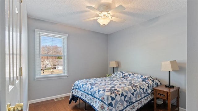 bedroom with a textured ceiling, wood finished floors, visible vents, and baseboards