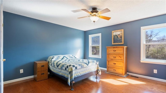 bedroom featuring visible vents, ceiling fan, baseboards, and wood finished floors