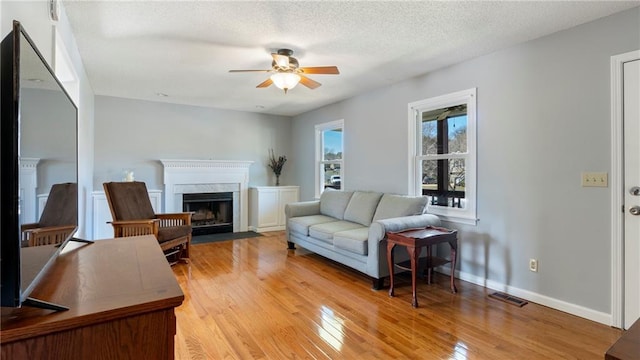 living room with visible vents, a premium fireplace, light wood-style floors, ceiling fan, and baseboards