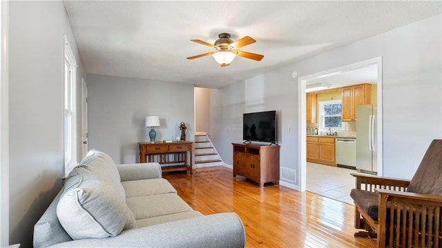 living area featuring light wood-style floors, ceiling fan, visible vents, and baseboards