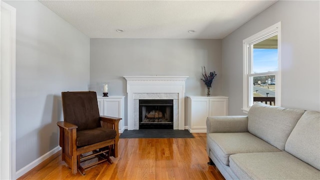 living area featuring a high end fireplace, baseboards, and light wood finished floors