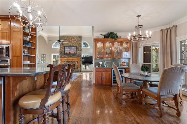 2160 Bradley Trl, Cumming, GA 30041 - dining room featuring a chandelier, beverage cooler, ornamental molding, a stone fireplace, and wood finished floors