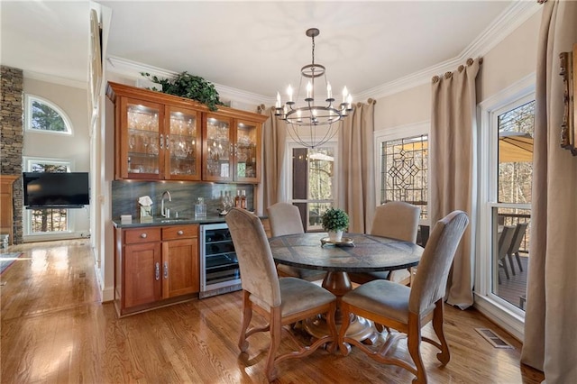 2160 Bradley Trl, Cumming, GA 30041 - dining space featuring beverage cooler, a chandelier, crown molding, light wood finished floors, and bar with sink