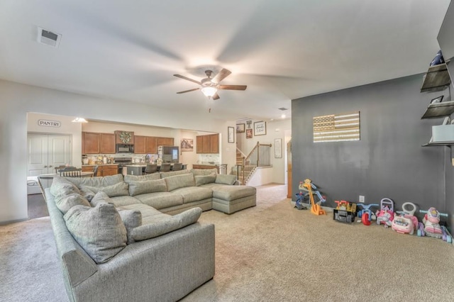 living room featuring light colored carpet, stairway, and ceiling fan